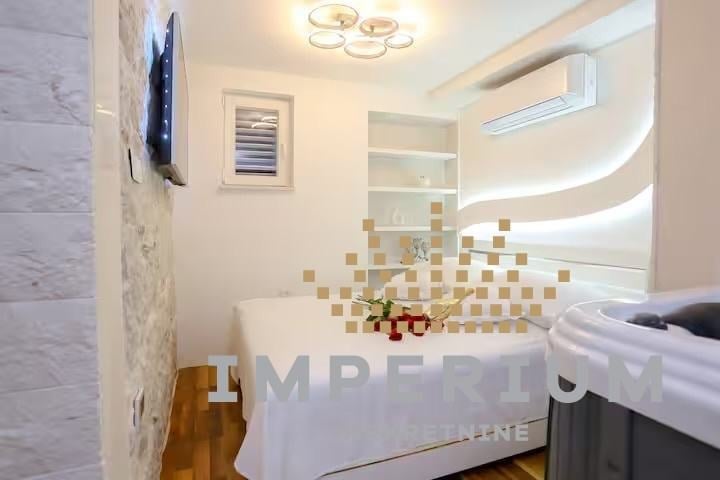 Modern bathroom interior with white bathtub, mosaic tile backsplash, illuminated shelving, ceiling light fixture, and mounted TV