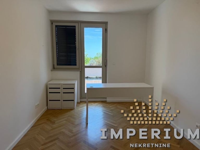Empty room with herringbone wooden floor, storage cabinet, glass door leading to terrace with lake view, and IMPERIUM logo with wooden blocks.