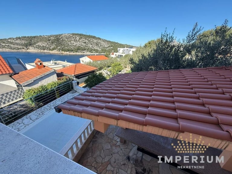 Rooftop view of red tile roof with Mediterranean lake and hills in background, featuring solar panels and waterfront property