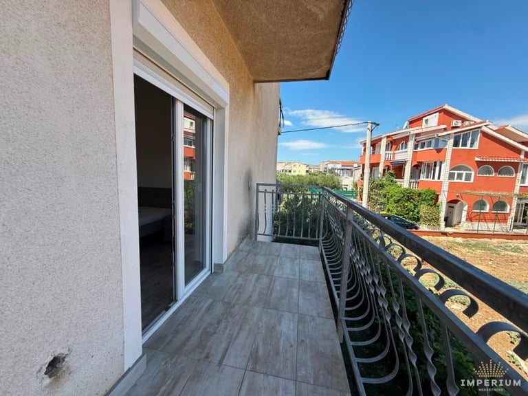 Modern apartment balcony with gray flooring and metal railings overlooking a residential area with orange-brick buildings