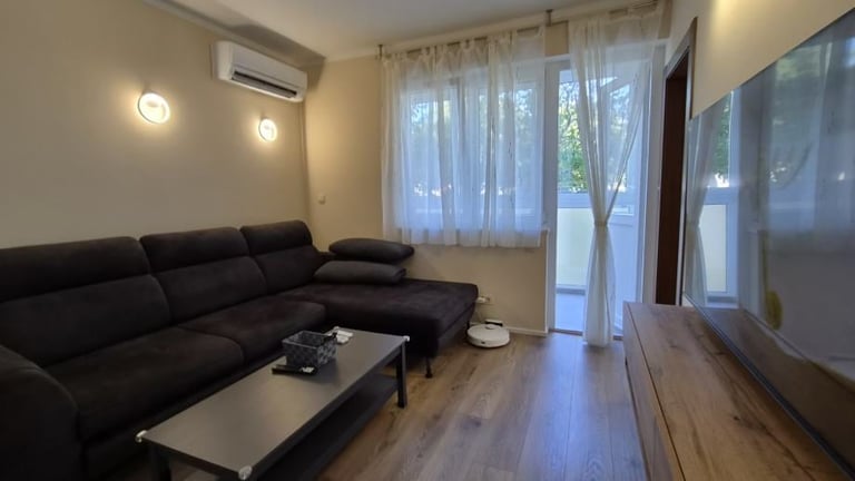 Modern living room with black sectional sofa, low coffee table, hardwood flooring, glass doors, and wall-mounted TV