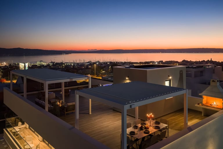 Modern rooftop terrace at twilight with waterfront views, contemporary architecture, ambient lighting, and lounge seating overlooking a bay at sunset