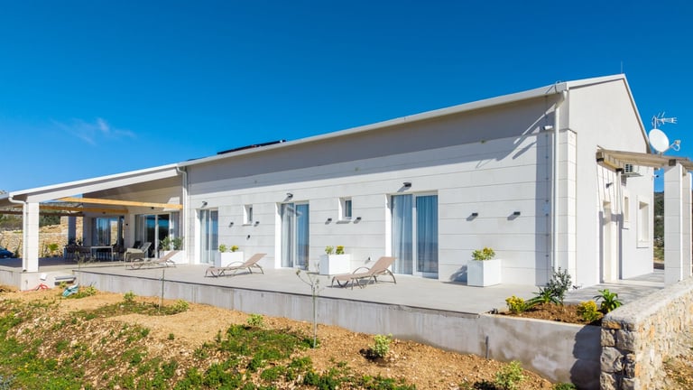 Modern white prefab house with covered porch under blue sky on rural property