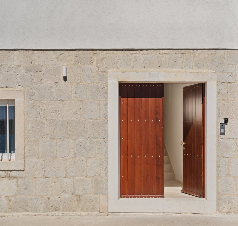Minimalist architectural photograph of a beige stone building facade with an open doorway revealing red wooden doors inside