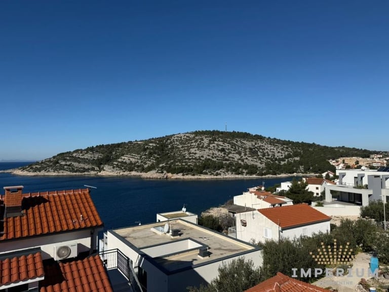 Coastal Mediterranean town with white buildings and red tile roofs overlooking a blue sea and forested hillside