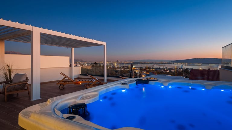 Illuminated rooftop pool with white pergola at dusk overlooking city skyline and mountains