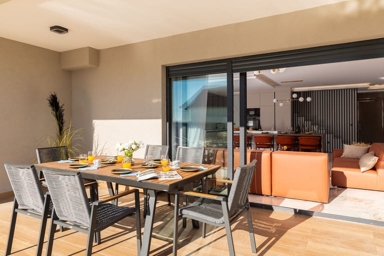 Modern dining area with black table and gray chairs, overlooking open-plan living space with orange sofa and glass doors