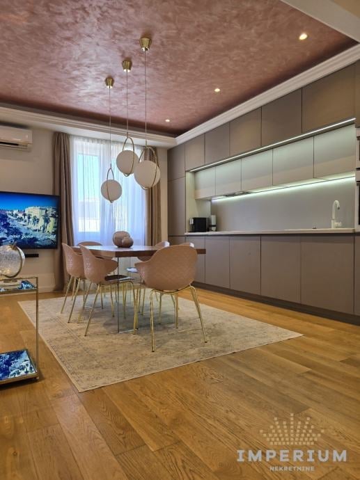Modern living room with dining area, tan pendant lights, wood flooring, contemporary furniture, and built-in kitchen cabinetry with lighting