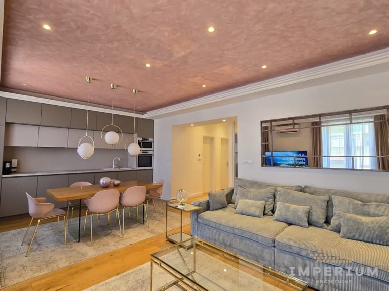 Modern open-concept apartment interior with dining area, kitchen, and living room with blue sofa and wood flooring