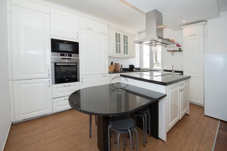 Modern white kitchen with black countertops, central island, built-in appliances, and wooden flooring