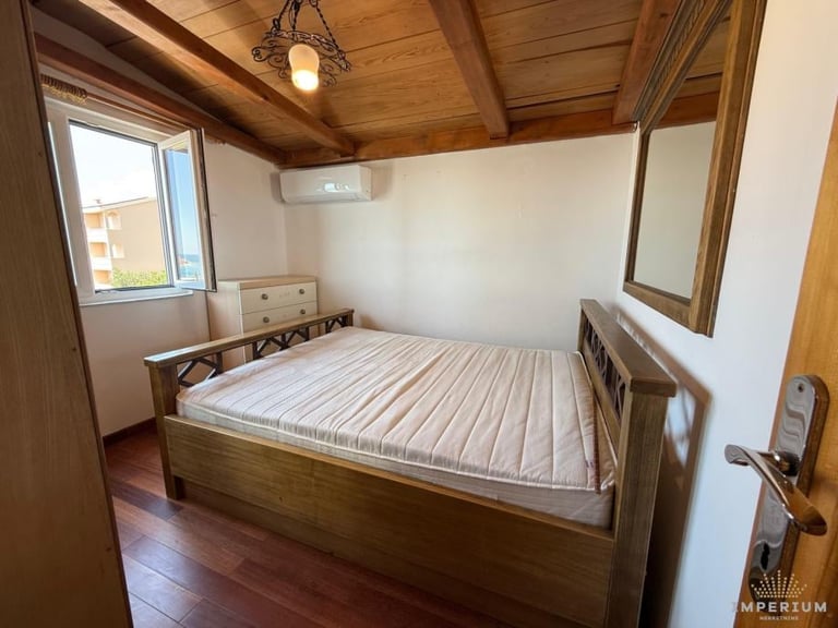 Wooden bedroom with a single bed with striped mattress, exposed wooden ceiling beams, window, and hardwood flooring