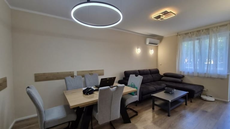 Modern open-plan living room with dining table, black sectional sofa, and work desk under circular ceiling lights