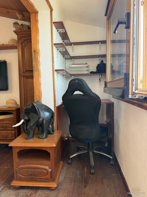 Small home office nook with black gaming chair, wooden desk with elephant statue, shelves above, and window on right