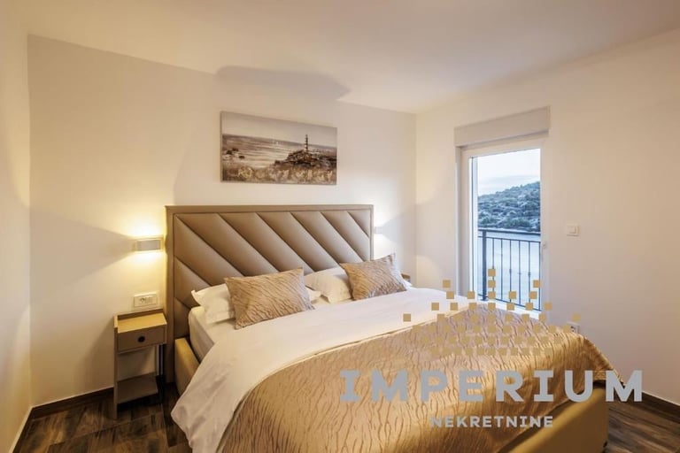 Modern bedroom with beige tufted headboard, white bedding, golden accents, side lamps, and mountain view through glass door with balcony