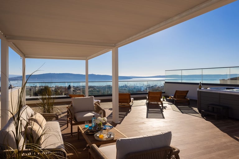Modern rooftop terrace with lounge seating, covered pergola, and panoramic ocean and mountain views