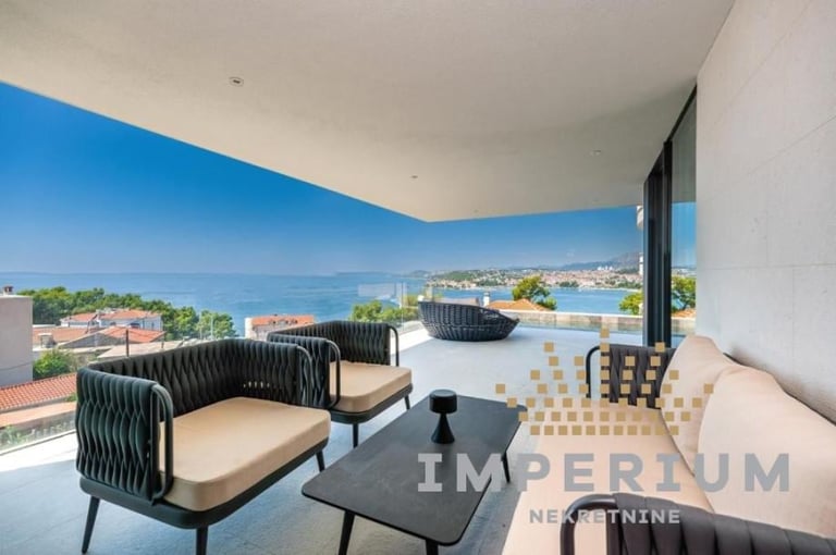 Modern waterfront terrace with lounge seating, black chairs, and panoramic sea and coastline views