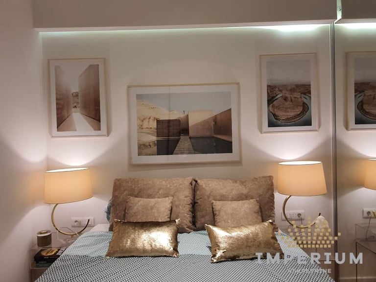 Modern bedroom with gold accent pillows, framed desert landscape photos, bedside lamps, and mirror reflecting the room