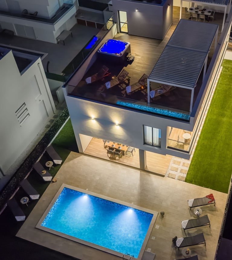 Aerial view of modern house with illuminated swimming pool and rooftop entertainment area with pool table at night