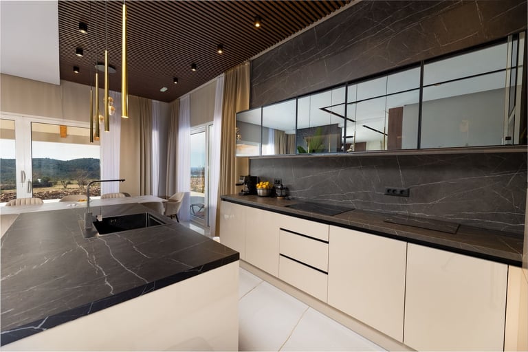 Modern luxury kitchen with white cabinetry, black marble countertops and backsplash, gold accents, and expansive windows overlooking a mountain landscape