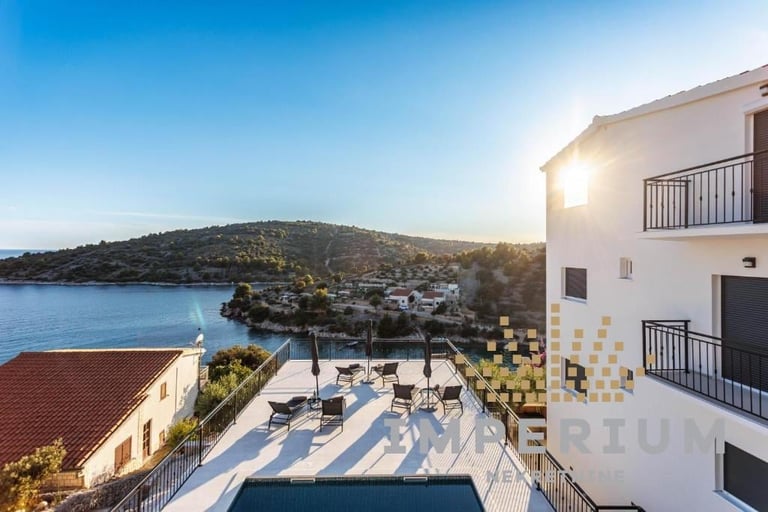 Luxury waterfront resort with pool deck overlooking Mediterranean bay and hillside village at sunset