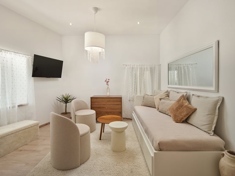 Modern bedroom with cream furnishings, mounted TV, wooden dresser, and lounge seating area