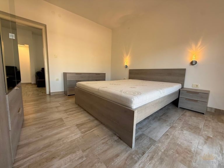 Modern bedroom with gray bed frame, white mattress, nightstands, wall sconces, wood flooring, and doorway to bathroom