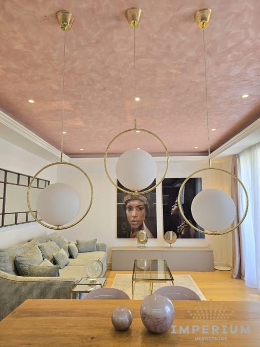Modern living room with three brass pendant lights featuring circular frames and frosted glass globes hanging from a pink textured ceiling.
