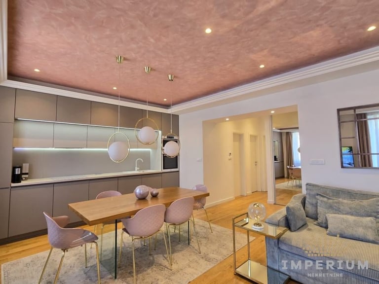 Modern open-plan living space with dining table, kitchen with gray cabinetry, and seating area with sofa and textured pink ceiling