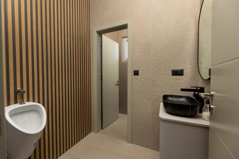 Modern bathroom interior with white toilet, black vessel sink, wooden wall panels, concrete textured walls, and gray door