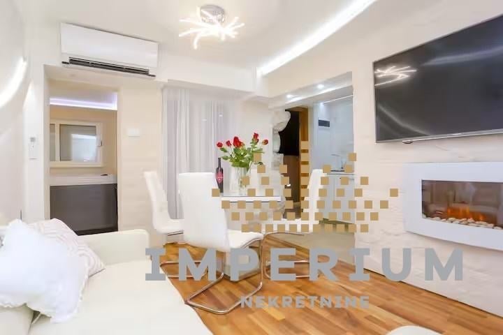 Modern luxury hotel suite with bed, fireplace, flat-screen TV, geometric tile accent wall, fresh flowers, and contemporary minimalist decor