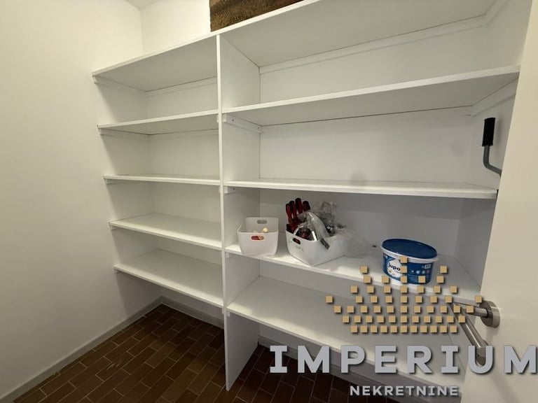 Empty white shelving unit with multiple shelves in a room, some items stored on bottom shelf including containers and boxes