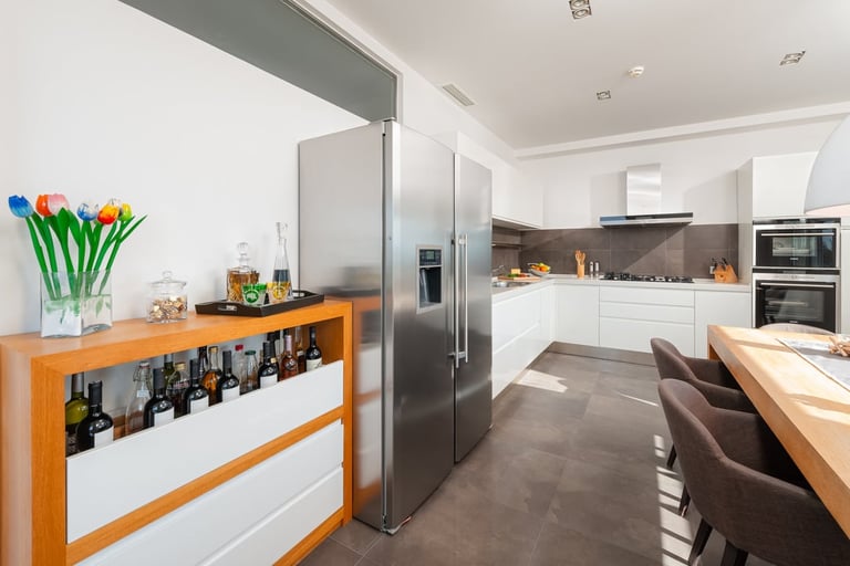 Modern open-plan kitchen with white cabinetry, stainless steel refrigerator, orange bar with wine storage, and dining area