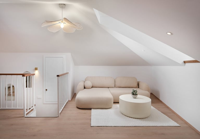 Modern attic bedroom with beige sectional sofa, round ottoman, white rug, sloped ceilings, and minimalist decor
