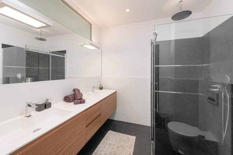 Modern bathroom with wood vanity, white countertop, large mirror, and walk-in shower with dark glass enclosure