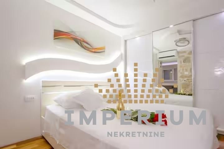Modern bedroom with curved white ceiling lights, decorative gold wall tiles, white bedding, and contemporary furnishings