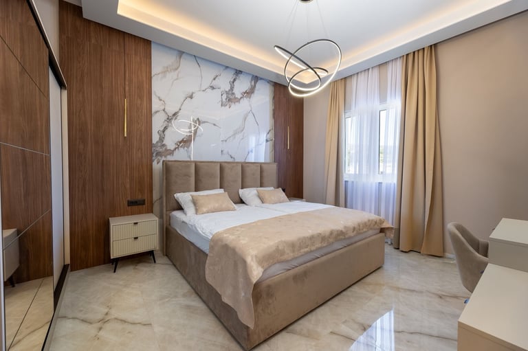 Modern bedroom with king-size bed, marble accent wall, warm lighting, wood paneling, and floor-to-ceiling windows with curtains