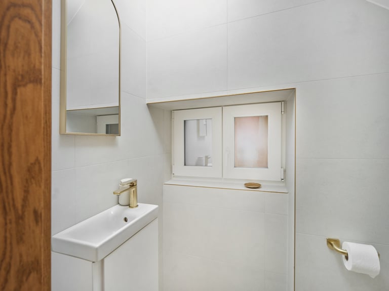 Modern bathroom with small rectangular sink, mirror cabinet, and window with frosted panes above beige wainscoting