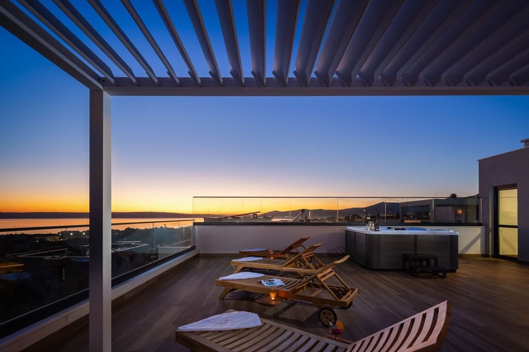 Modern rooftop terrace at dusk with lounge chairs, pergola, hot tub, and panoramic water and city views at sunset
