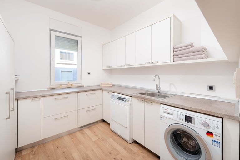 Modern utility room with white cabinetry, wooden countertops, integrated white dishwasher, and front-loading washing machine on wooden flooring