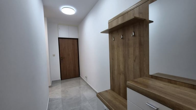 Modern entryway with wooden coat rack and bench against white walls, dark wooden door, and ceiling light