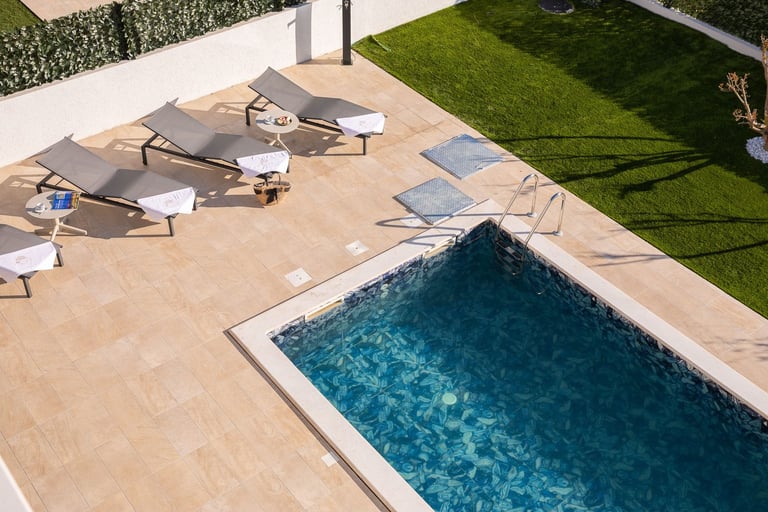 Aerial view of a swimming pool with lounge chairs on a beige deck and green lawn in the background