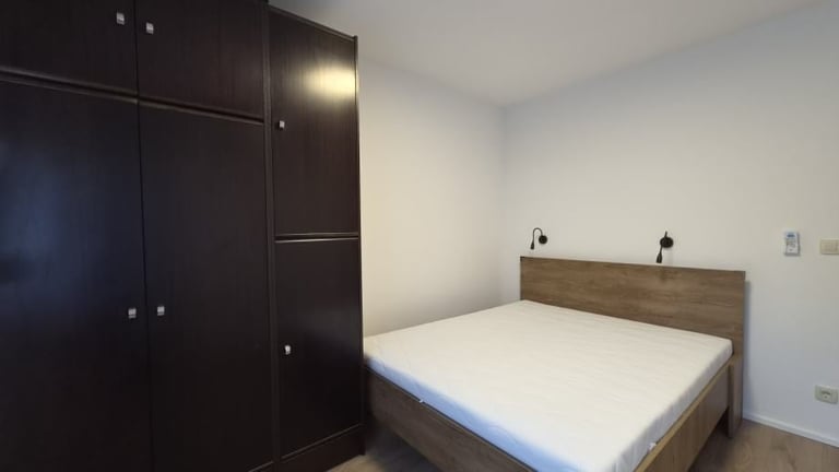 Modern bedroom with wooden bed, white bedding, black wardrobe, and wall sconces on light walls