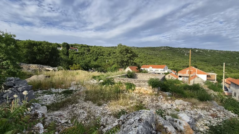 Rural settlement with red-roofed buildings nestled among rocky terrain and green vegetation under a partly cloudy sky