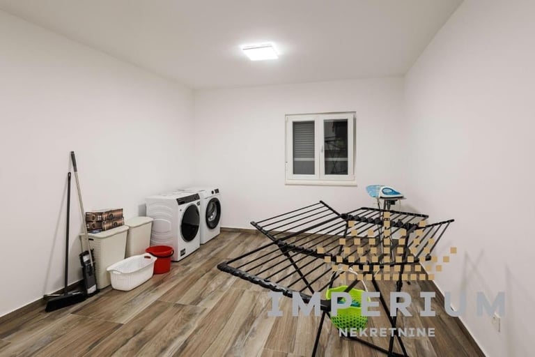 Empty utility room with wooden flooring, front-load washers, ironing board, and furniture frame ready for assembly