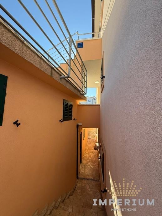 Narrow alleyway between orange and white buildings with metal railings overhead and a doorway visible in the distance.