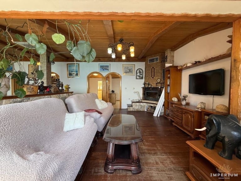 Cozy living room with beamed wooden ceiling, pink sofa, TV, decorative plants, and warm amber lighting
