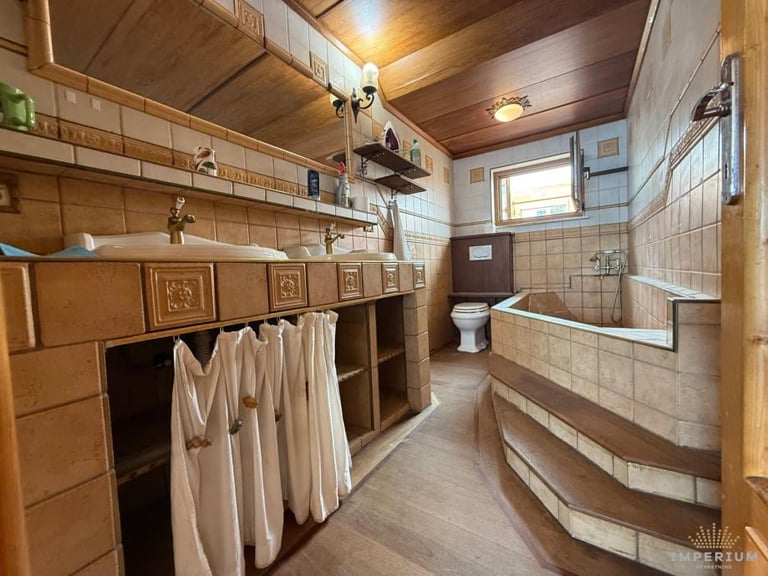 Vintage bathroom with wooden cabinetry, white subway tiles, curved bathtub, hanging towels, and warm lighting from wooden ceiling
