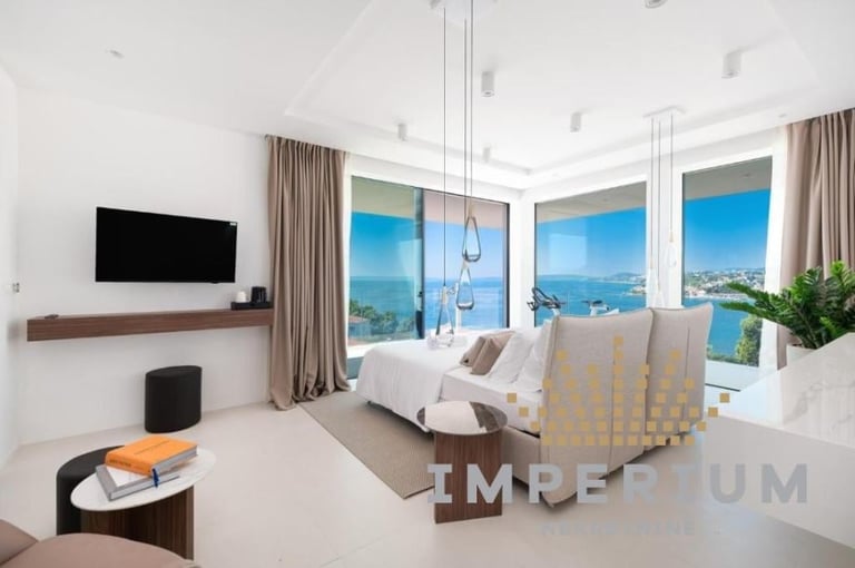 Modern luxury bedroom with ocean view, floor-to-ceiling windows, floating TV, pendant lights, and contemporary furnishings overlooking blue water