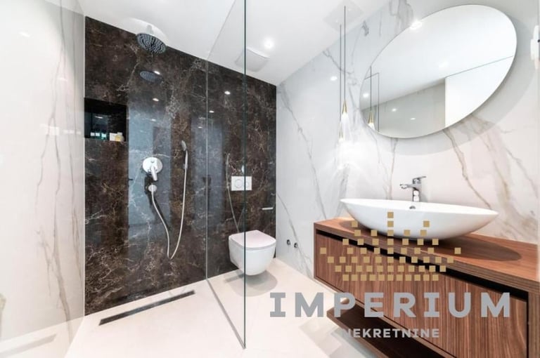 Modern bathroom with dark marble walk-in shower, round mirror, wooden vanity with vessel sink, and white walls