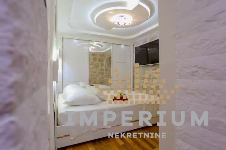 Modern bedroom with white platform bed, marble accent walls, circular ceiling light fixture, and glass shower enclosure with tiled interior
